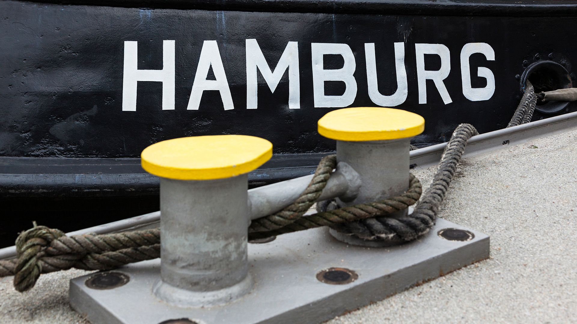 Die Schrift "HAMBURG" steht auf einem schwarzen Schiffsbug. Davor sind zwei Poller.