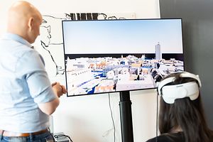 Zwei Personen vor einem digitalen Stadtmodell. Eine Frau trägt eine VR-Brille.