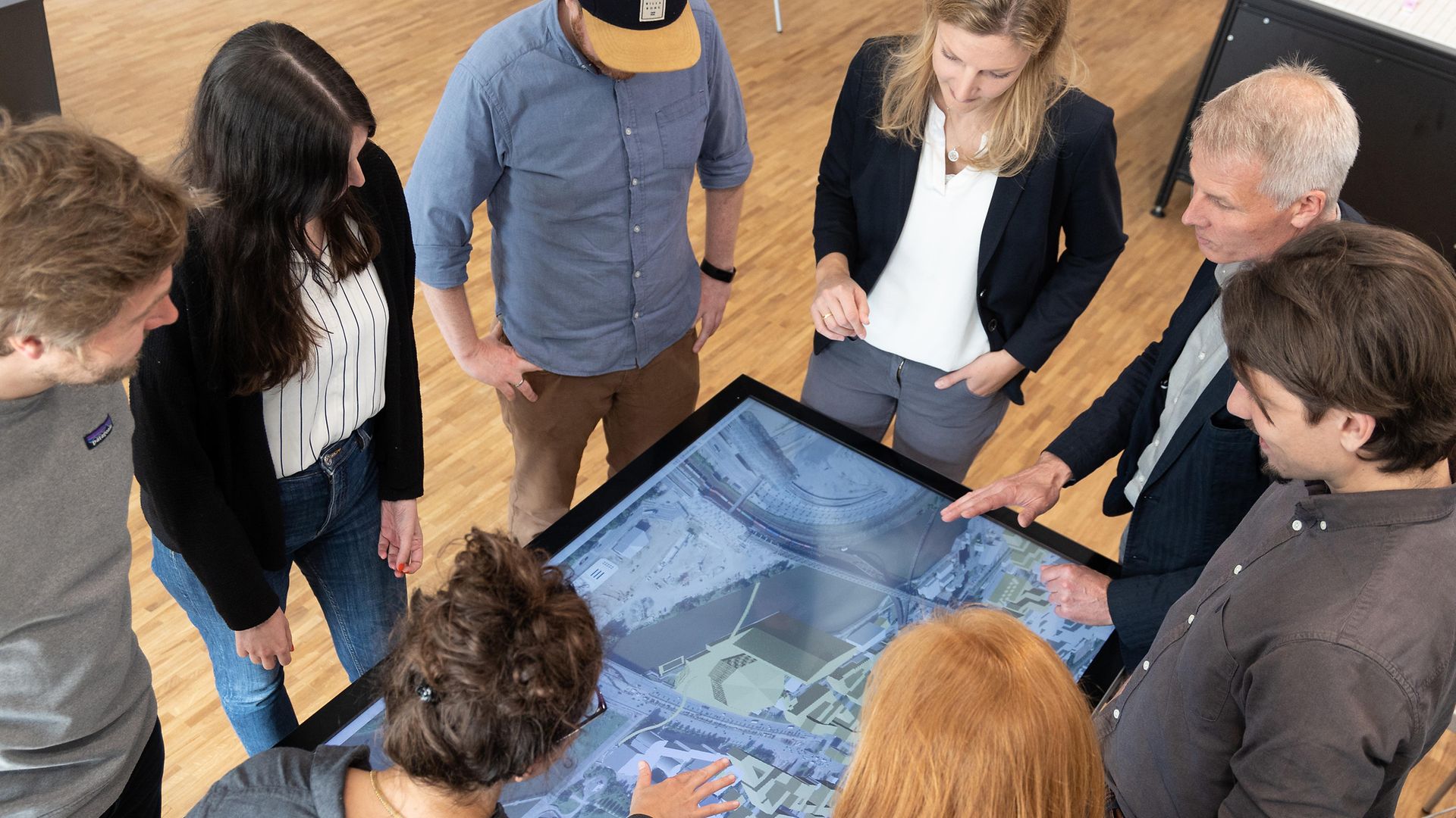 Eine Gruppe von Menschen steht um einen digitalen Tisch mit Stadtmodell herum.